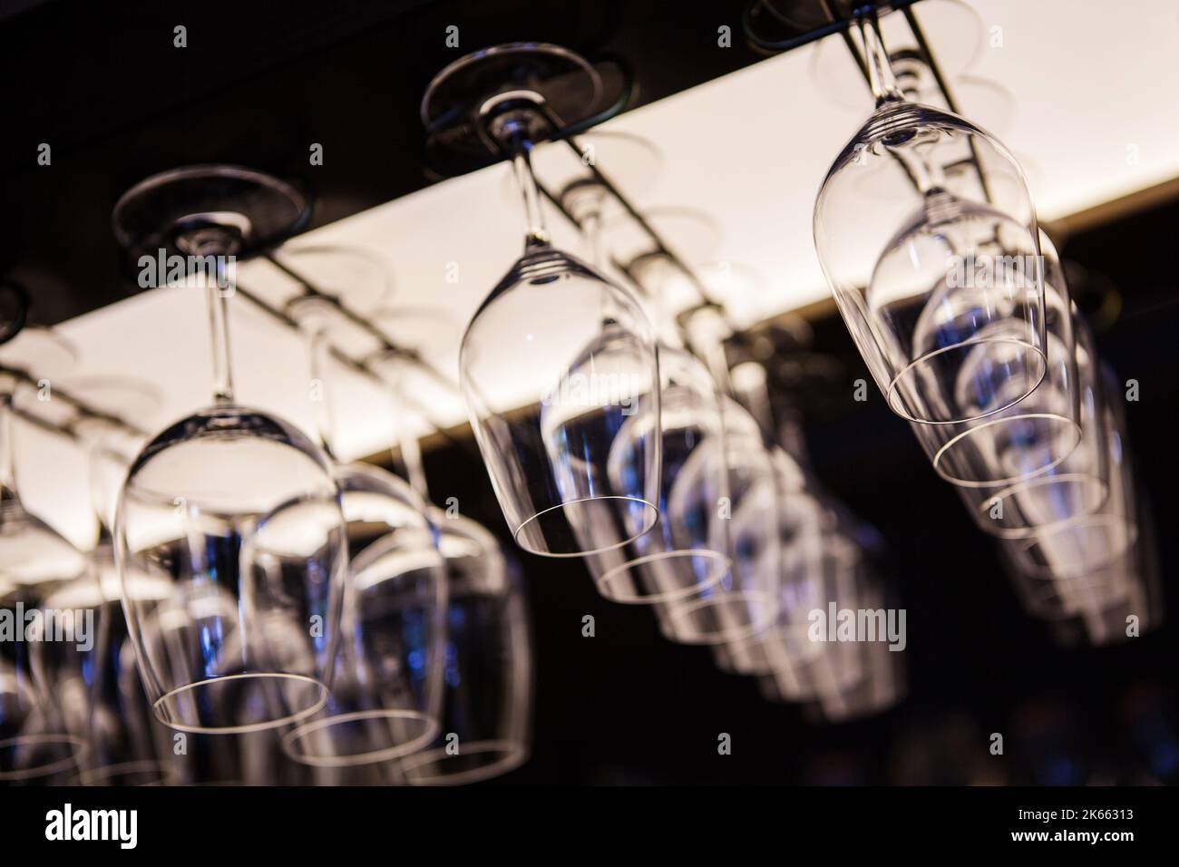 Empty wine glasses hanging upsidedown in bar interior. Stock Photo
