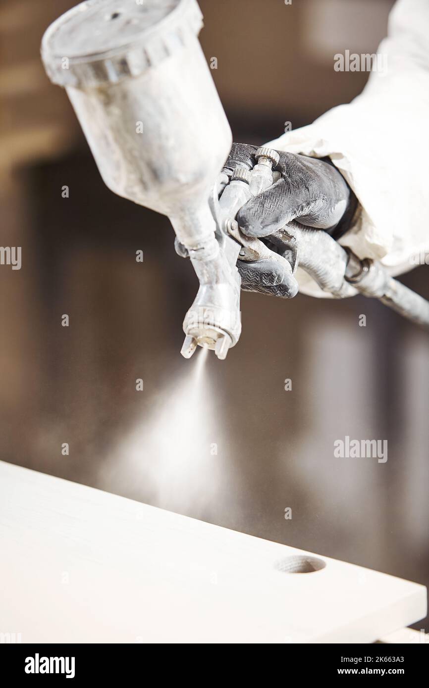 Vertical close-up of industrial worker using paint gun or spray gun for applying paint, airless spraying. Stock Photo