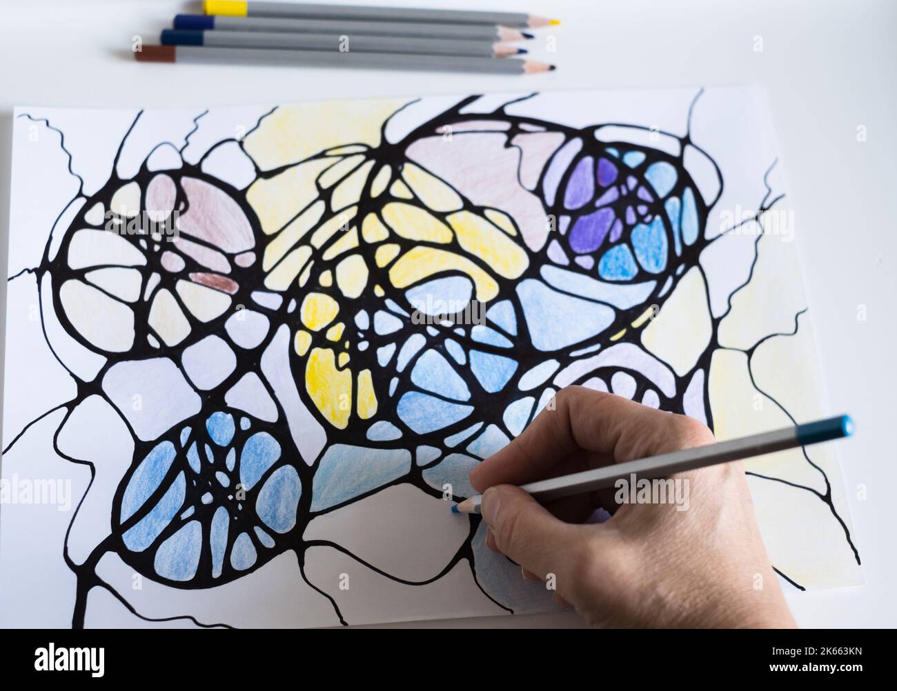 A woman draws a neurographic drawing on paper with color pencils. Neurographic art is an easy way to work with the subconscious mind through drawing. Stock Photo