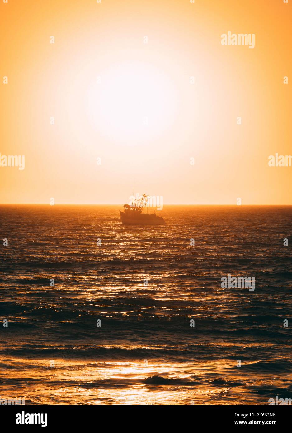A vertical shot of the wavy sea with a floating single boat at sunset ...