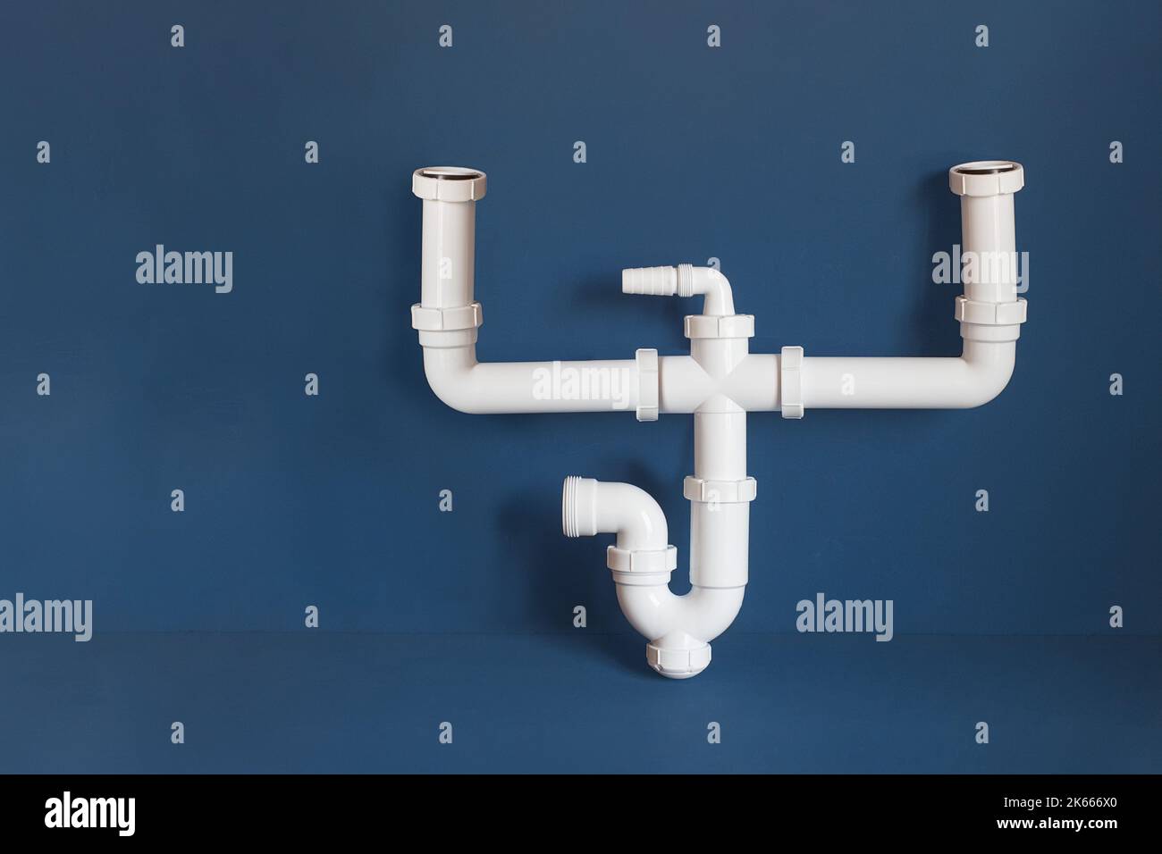 An isolated assembled double adjustable sink siphon for a 2-bowl sink with a horizontal outlet on a colorful blue studio background with copy space. B Stock Photo
