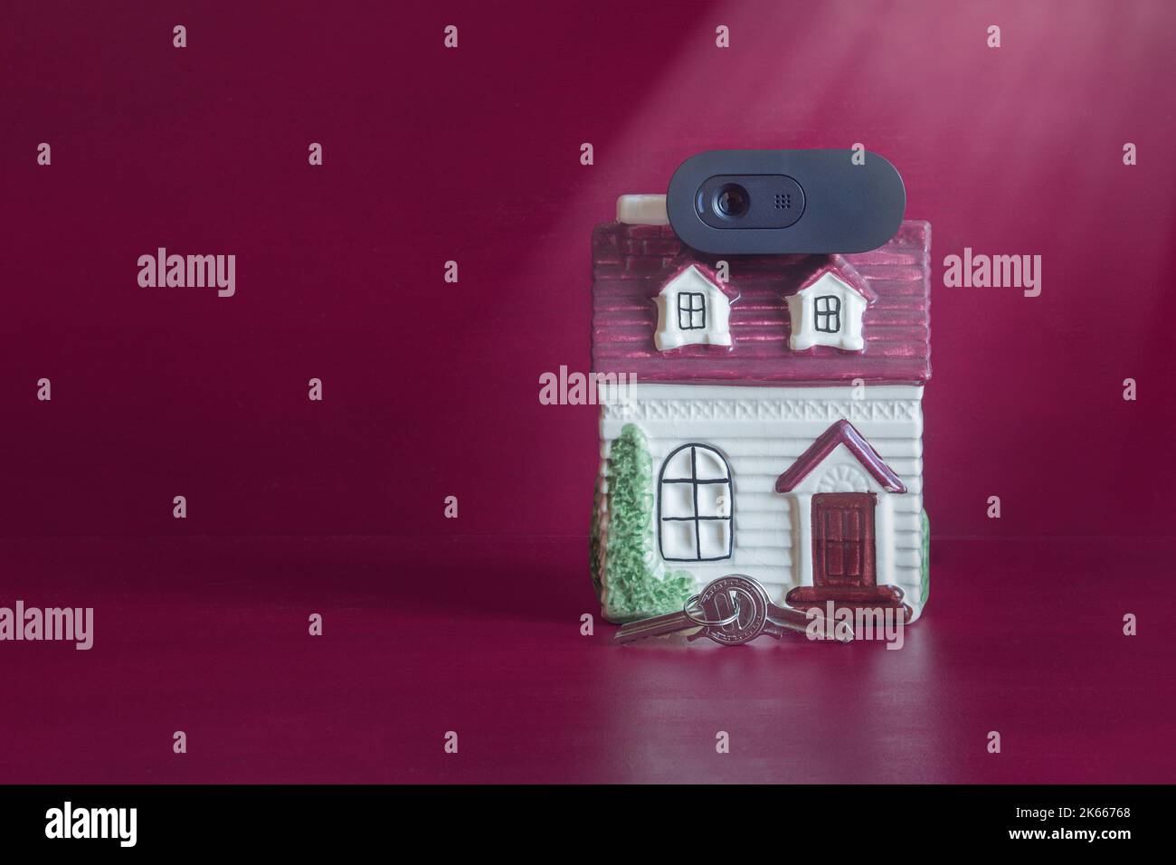 A pair of keys held together by a ring in front of the door of an old painted ceramic house with a webcam on the tiled roof. Concept of home and secur Stock Photo