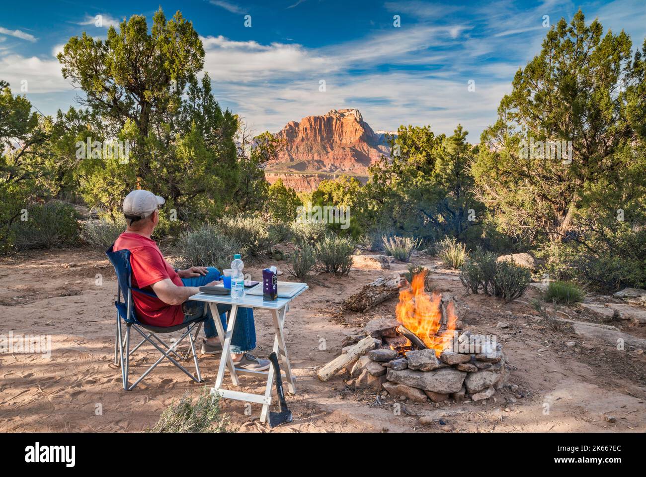 Man at camp fire at sunset, in pinyon juniper forest off Smithsonian Butte Road, Canaan Mtn Wilderness, Mount Kinesava in Zion Natl Park in dist, Utah Stock Photo