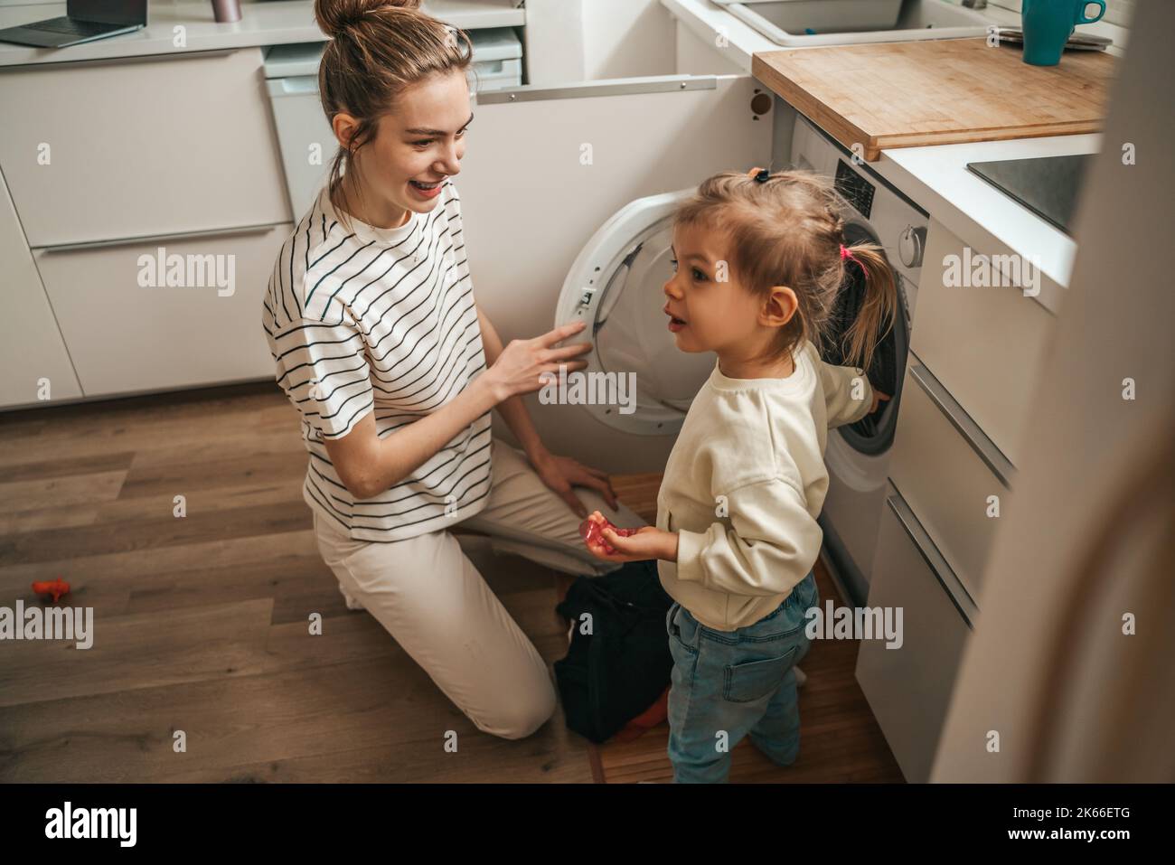 Female and her child putting dirty clothes into the washer Stock Photo