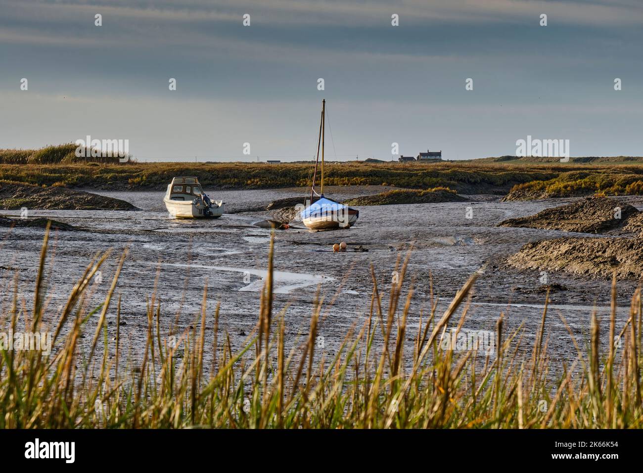 Boats at low tide at Brancaster Staithe, with the Royal West Norfolk Golf Club house at Brancaster in the distance, Norfolk Stock Photo