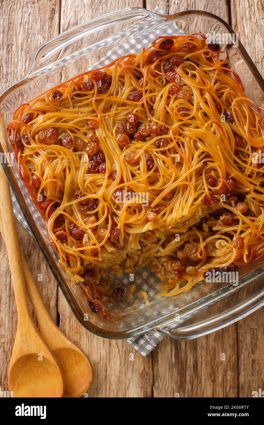 Caramelized Noodle and Pepper Yerushalmi Kugel with raisins close-up in a glass bowl on the table. Vertical top view from above Stock Photo