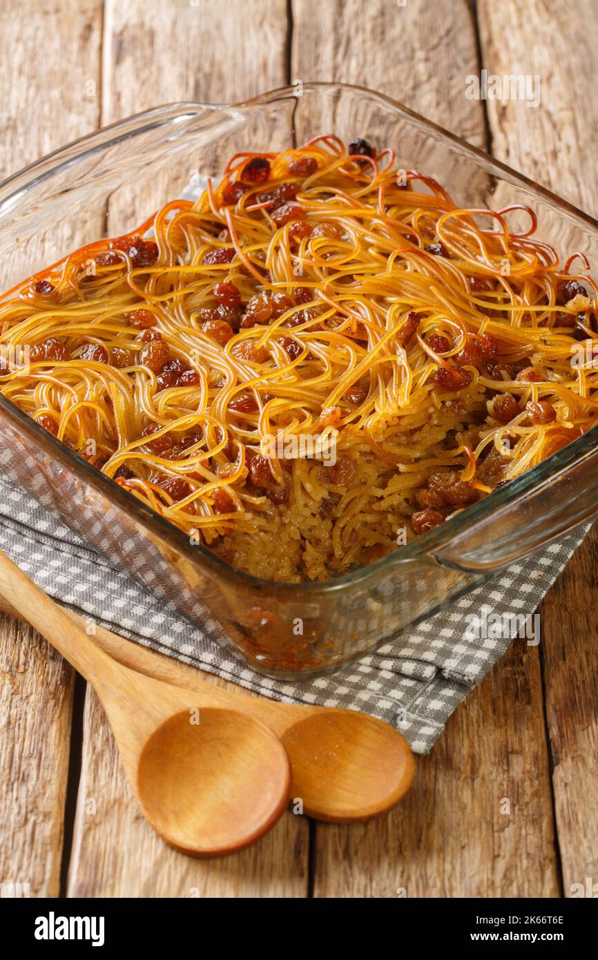 Caramelized Noodle and Pepper Yerushalmi Kugel with raisins close-up in a glass bowl on the table. Vertical Stock Photo