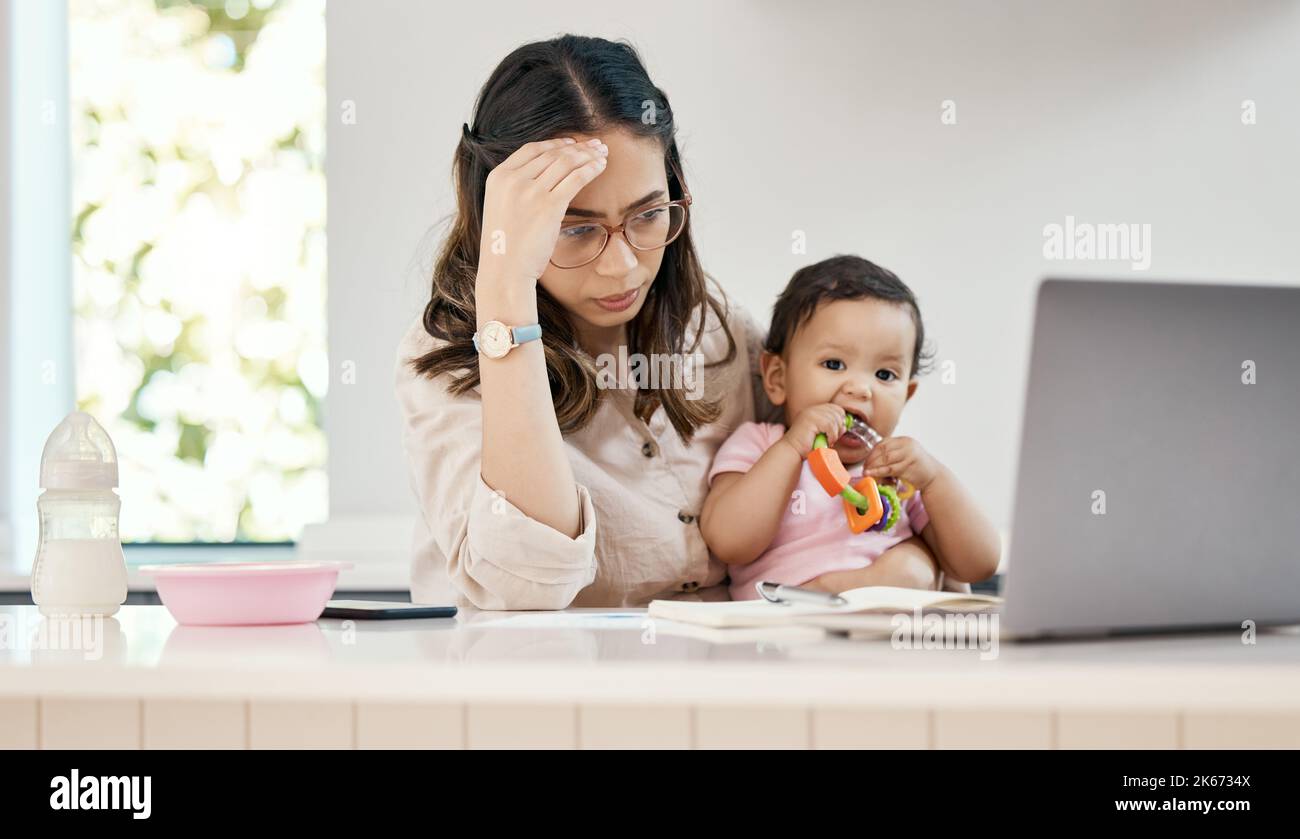 Every day is different with its own challenges and blessings. a woman looking stressed while sitting with her laptop and her baby on her lap. Stock Photo
