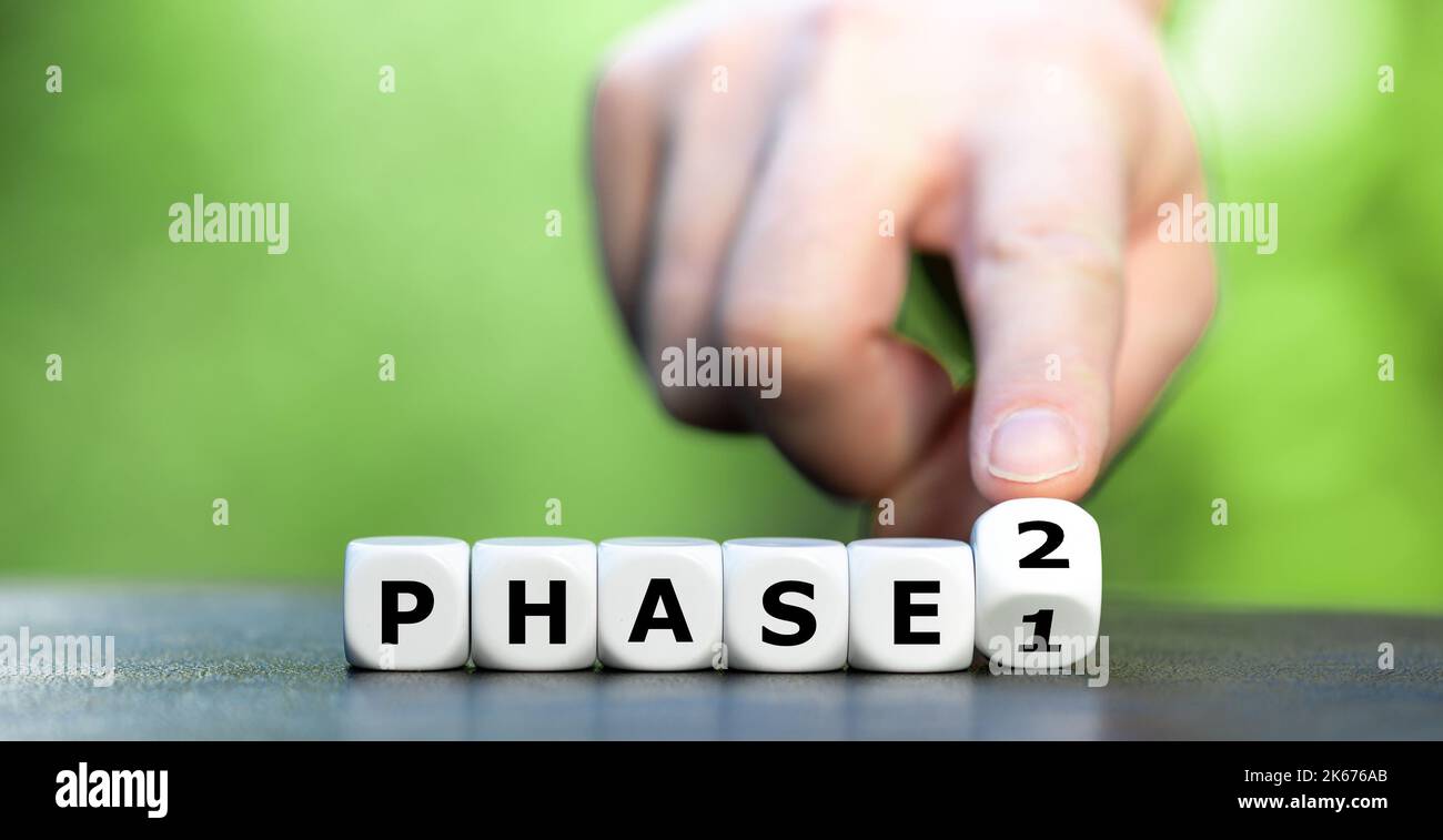 Hand turns dice and changes the expression 'phase 1' to 'phase 2'. Stock Photo