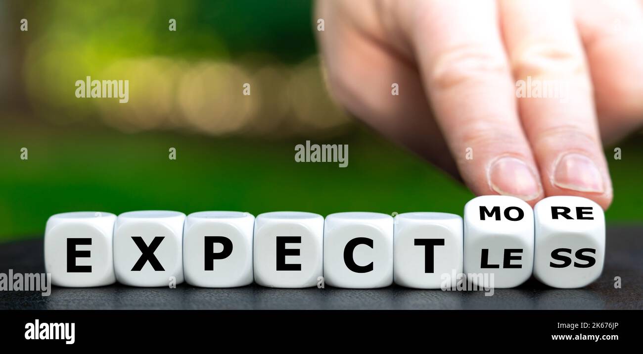 Hand turns dice and changes the expression 'expect less' to 'expect more'. Stock Photo