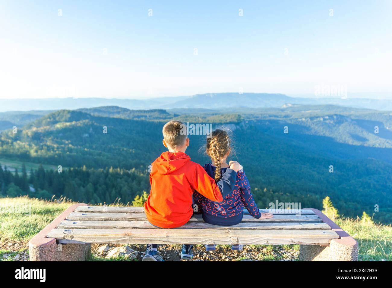 Sister and brother are hugging on a bench with a view of the mountain valley. Concept of family love, friendship, protection and care Stock Photo