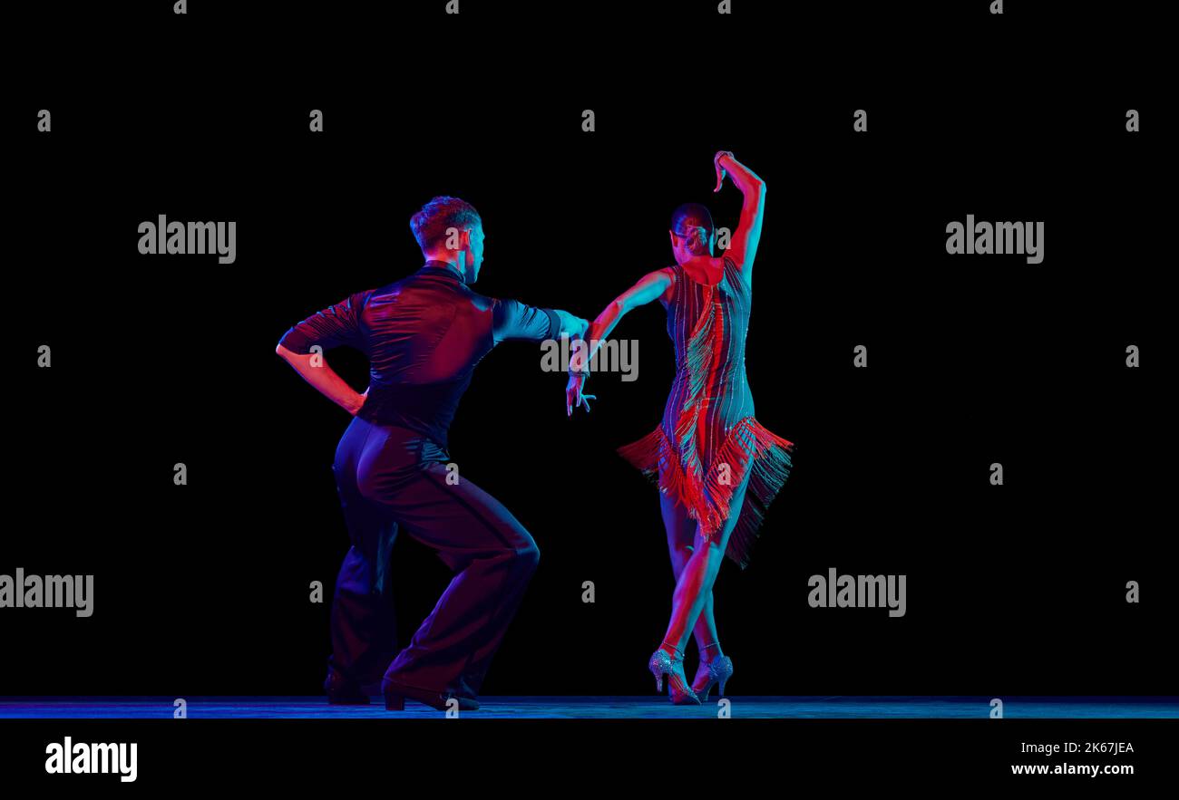 Two dancing people, ballroom dancers in elegance outfits in motion, action over dark background in neon light. Concept of art, music, dance, emotions. Stock Photo