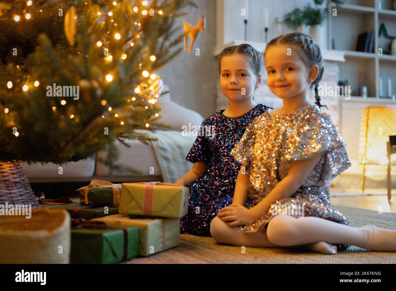 Two cute little girls under Christmas tree. Children under Christmas tree with gift boxes. New Year's decorations. Sisters Stock Photo