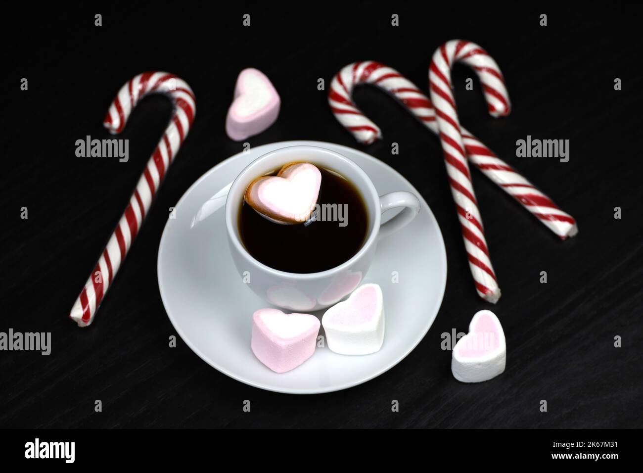 White cup of coffee or tea with marshmallow hearts and candy canes on dark wooden table. Hot drink with sweets for Christmas holidays Stock Photo