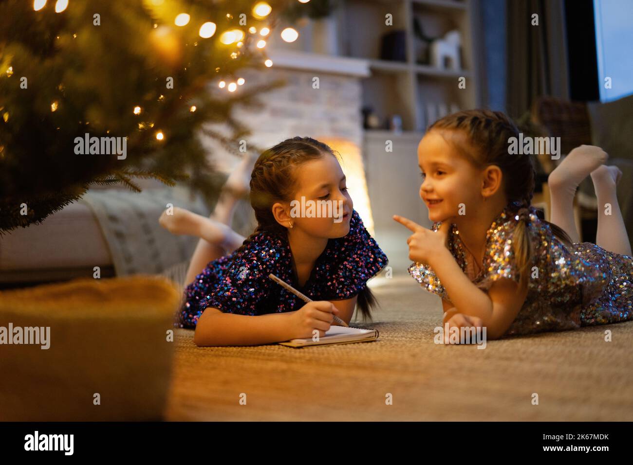 Merry Christmas and Happy Holidays. Two little girls write the letter to Santa Claus near Christmas tree indoors Stock Photo