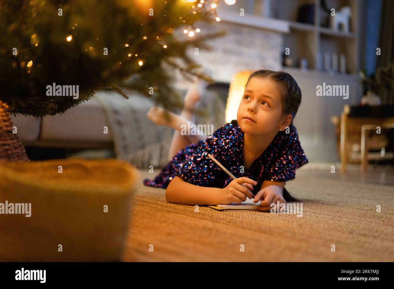 christmas, holidays and childhood concept - smiling girl making wish list or letter to santa at home Stock Photo
