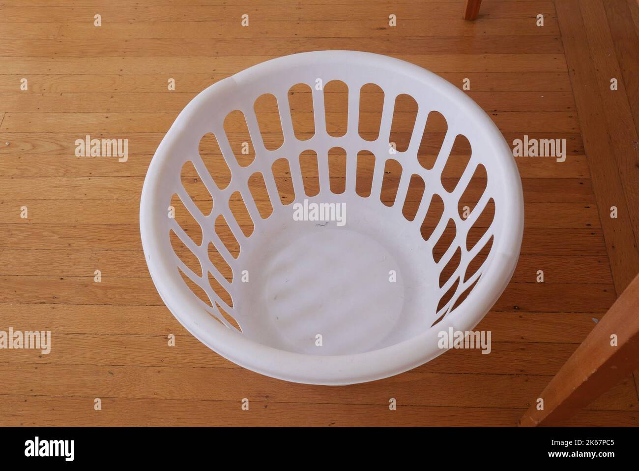 An empty white plastic laundry basket on wooden floors. Stock Photo
