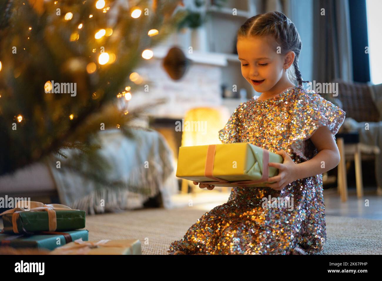 Happy holidays. Little child opening present near Christmas tree. The girl laughing and enjoying the gift. Stock Photo