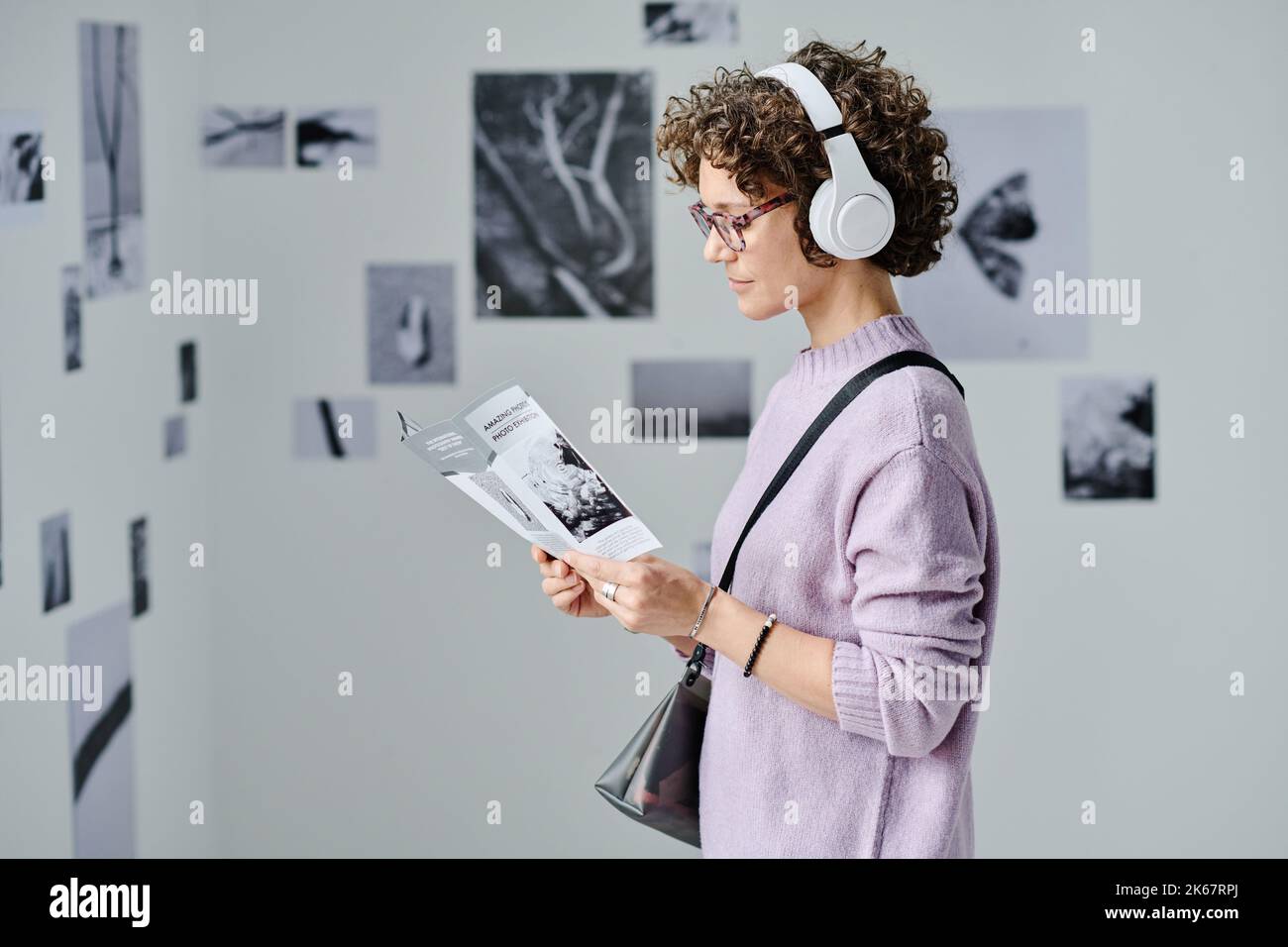 Young woman in wireless headphones reading booklet while standing at