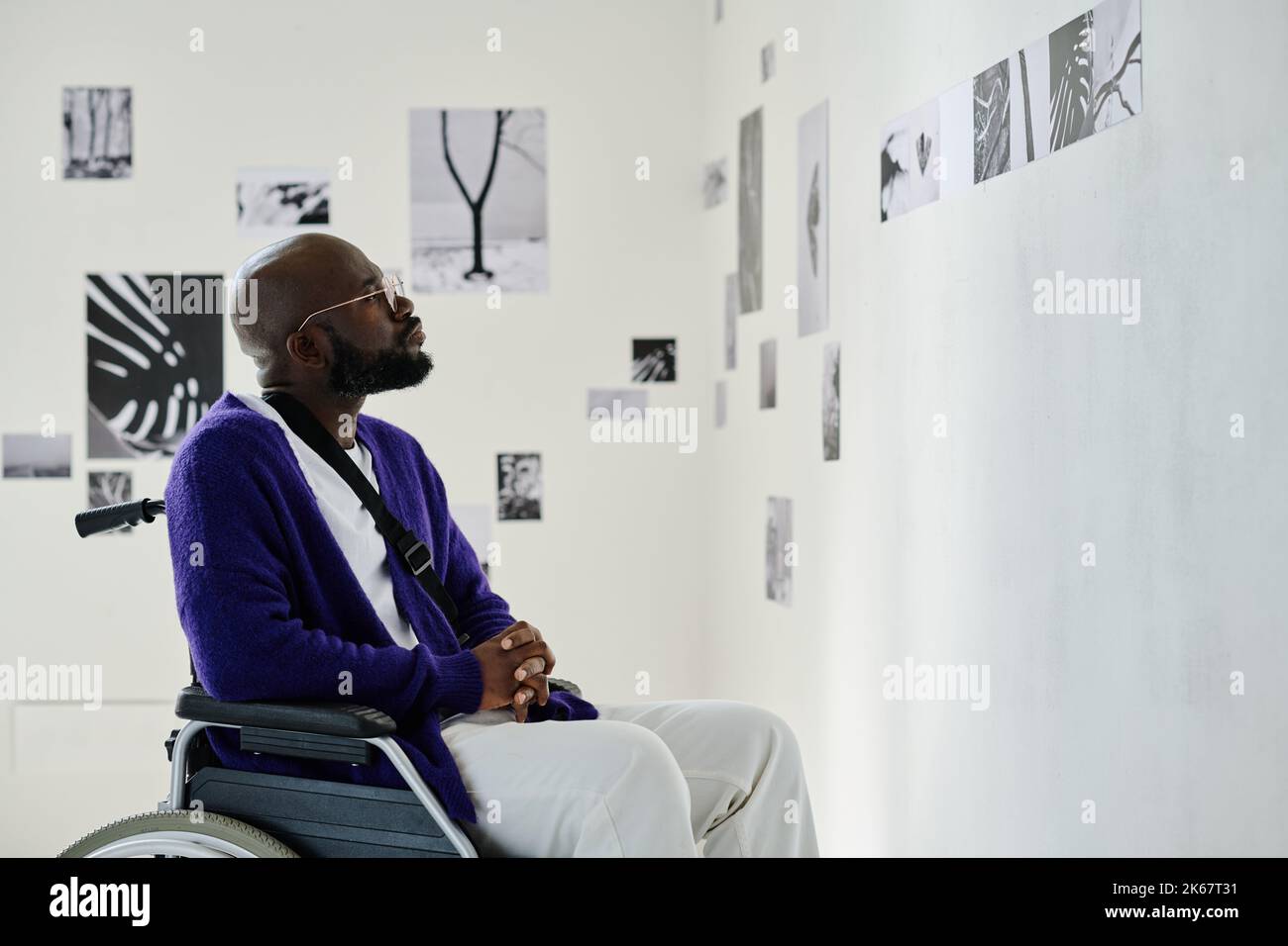 African young man with disability sitting in wheelchair visiting exhibition at art gallery Stock Photo