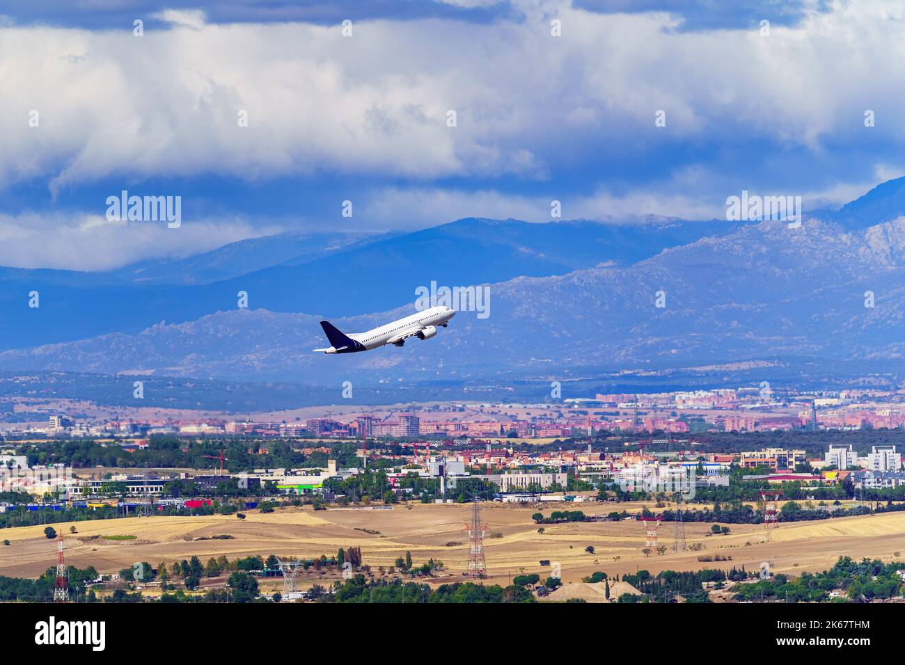 Generic Avio taking off and taking height next to a city and large mountains in the background. Stock Photo