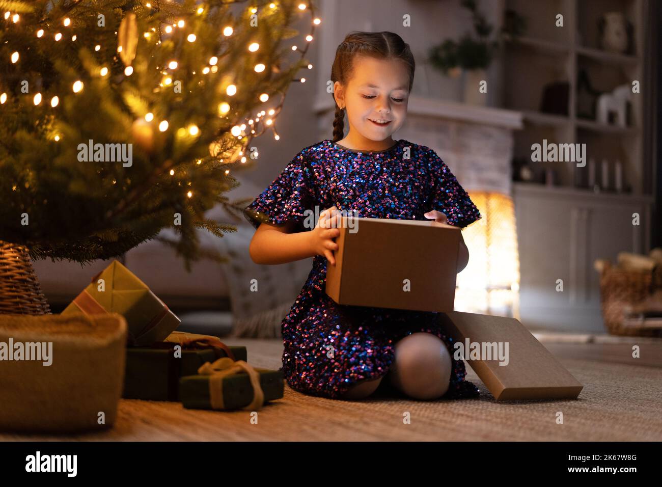 Merry Christmas. happy girl with magic gift at home near Christmas tree and fireplace. Stock Photo