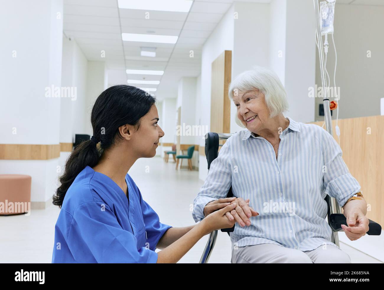 Psychological support from nurse to elderly woman sitting in wheelchair on corridor of medical clinic. Caring for people with disabilities at hospital Stock Photo