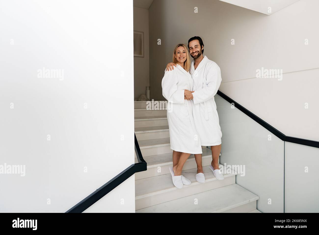 Spa family day. Handsome man with his beautiful wife in white bathrobes enjoying spa weekend while honeymoon walking at wellness center Stock Photo