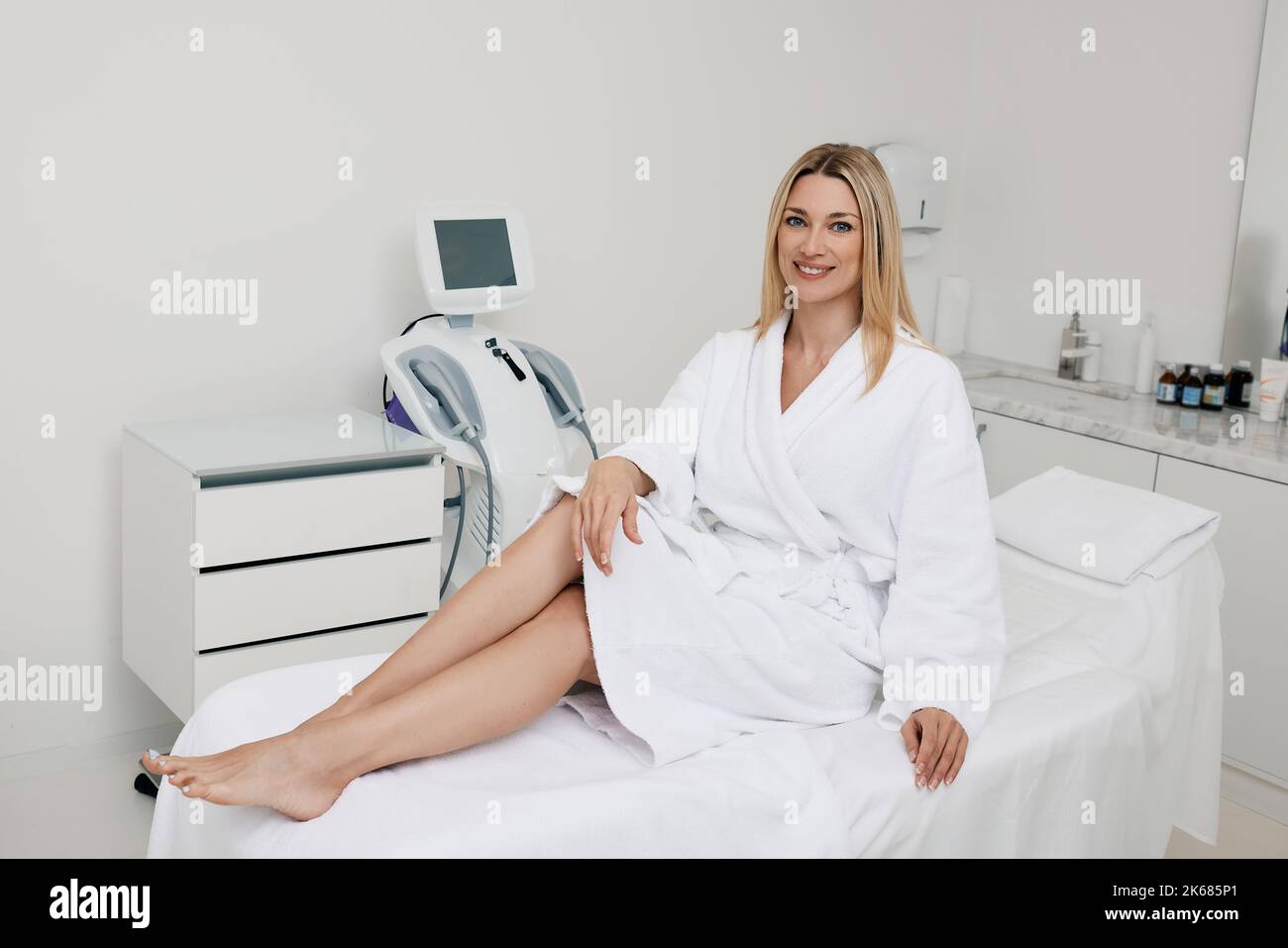 Beautiful woman is sitting on couch in hardware cosmetology cabinet in spa center before starting session of procedures for her body. Hardware cosmeto Stock Photo