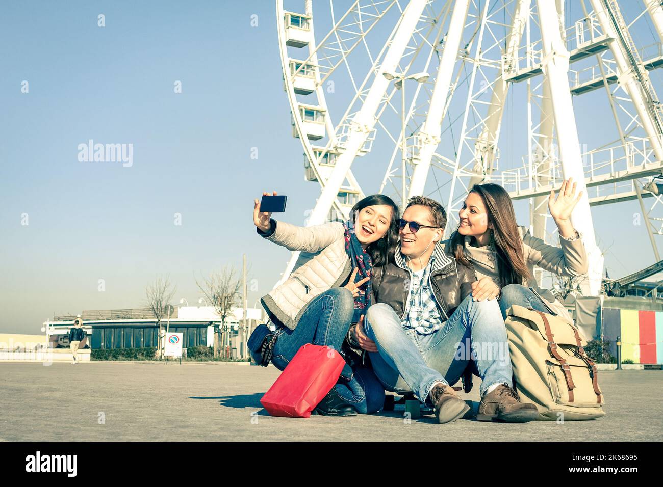 Young hipster people taking a selfie at luna park with ferris wheel - Concept of friendship and fun with new trends and technology - Best friends catc Stock Photo