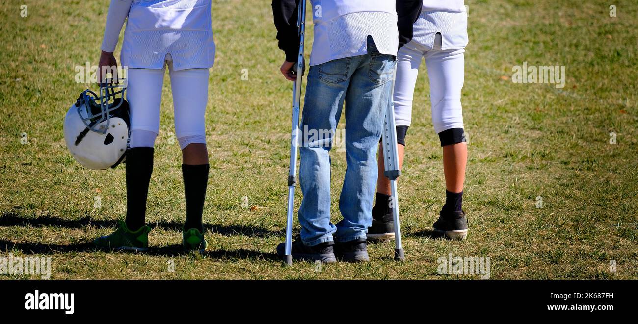 Injured football player on sidlines of game with crutches by team Stock Photo