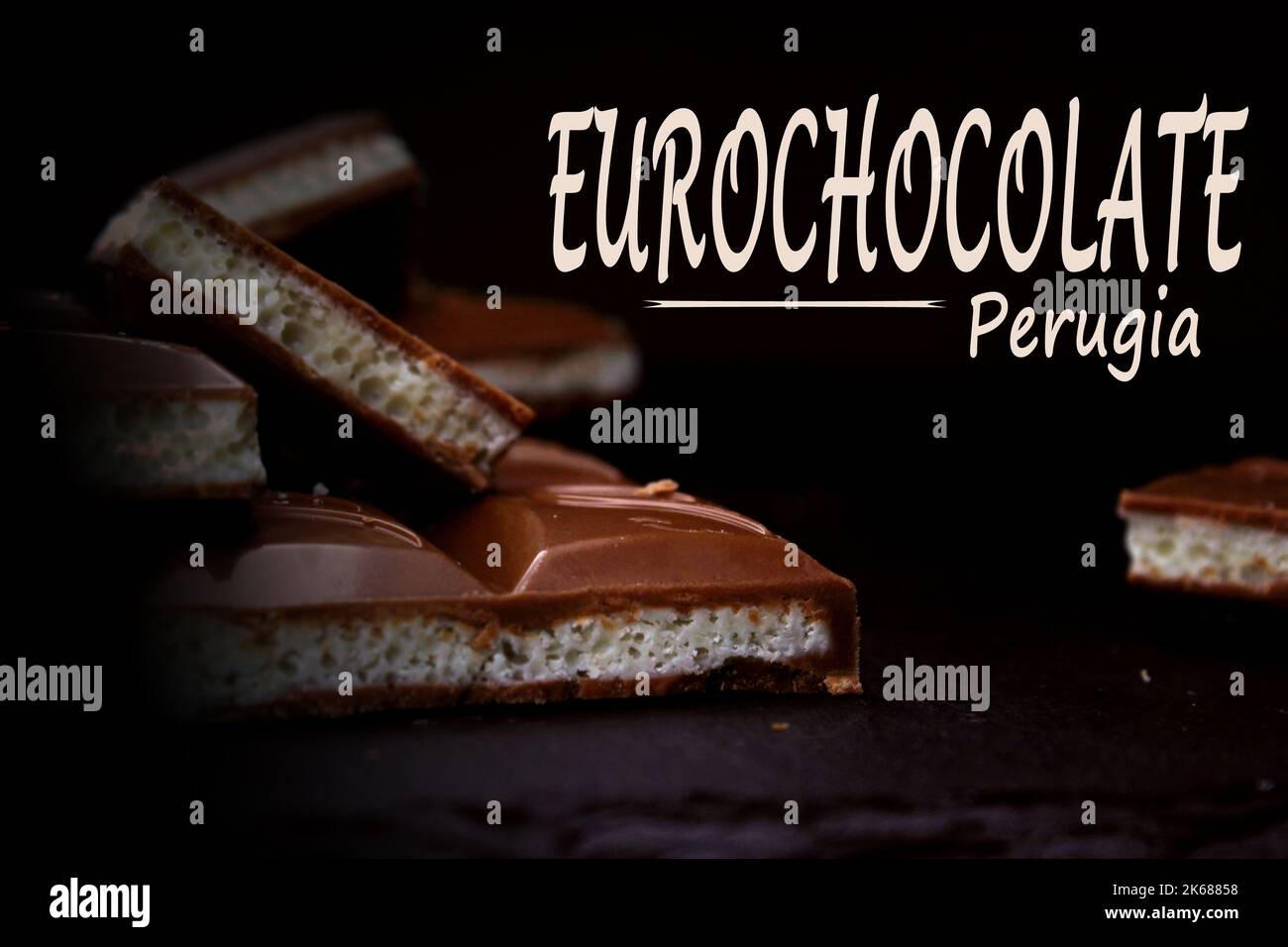 Pieces of milk aerated chocolate close-up on a dark background with an inscription. The concept of the Perugia Chocolate Festival. Stock Photo