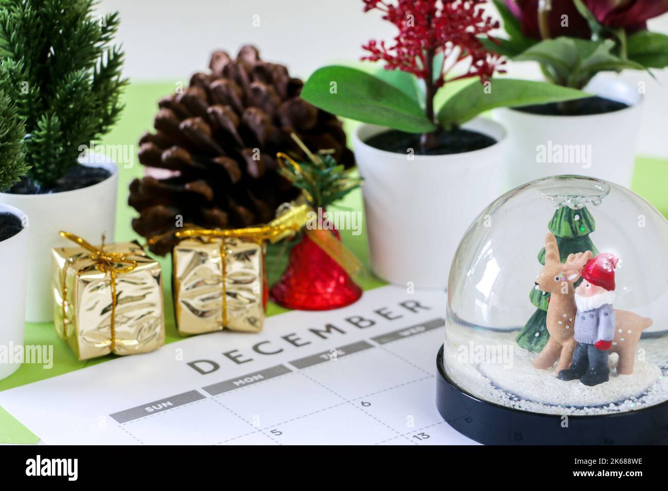 Christmas concept, festive snow globe on December calendar, out of focus in background are decorations such as plants, pine cone, gold wrapped gifts, Stock Photo