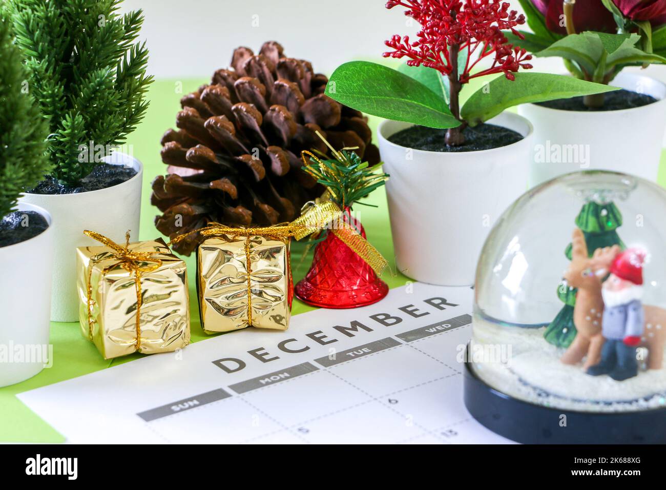 Christmas concept, December calendar along with Christmas decorations such as plants, pine cone, gold wrapped gifts and a shiny red bell, with snow gl Stock Photo