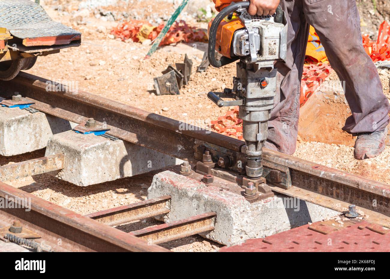 construction of railway track with wooden sleepers. Worker screws the bolt that connects the rail to the concrete sleeper with a special tool Stock Photo