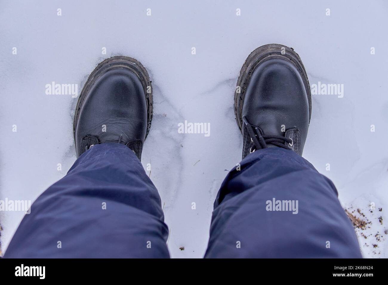 Women feet in black boots treading snow as seen from above. Top view, Copy space, wintertime Stock Photo