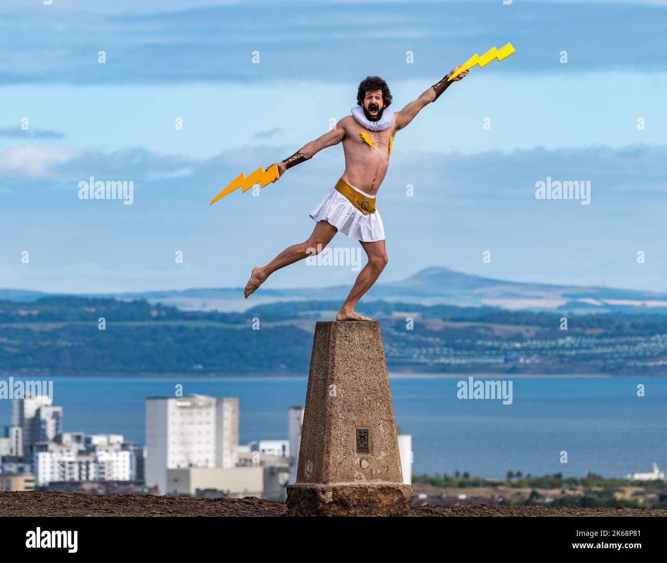 Fringe performer Garry Starr aka Damien Warren-Smith as Greek God Zeus with lightning bolts on a trigpoint, Calton Hill, Edinburgh, Scotland,UK Stock Photo