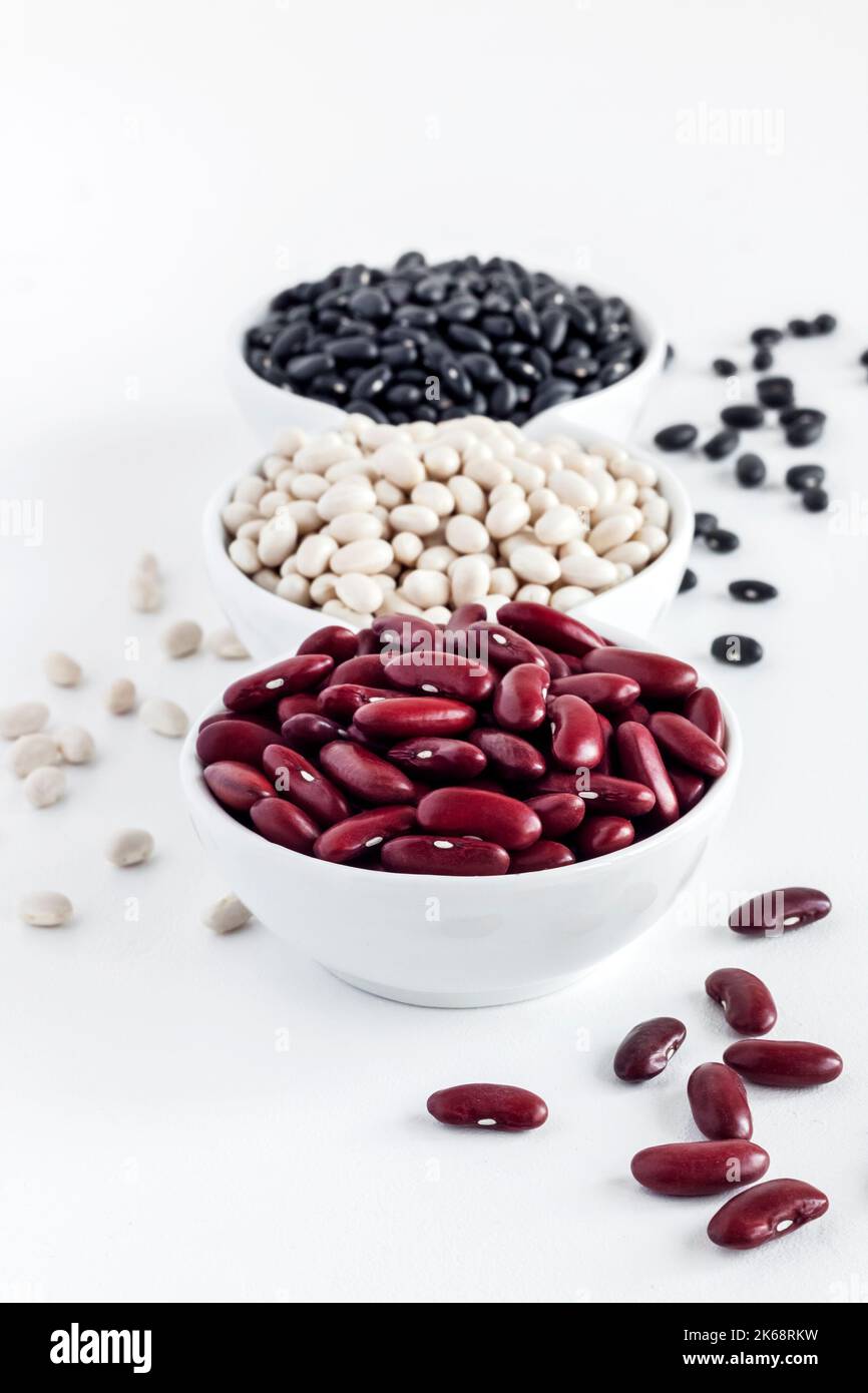 Assortment of beans in a white bowl on white background. Red kidney beans, white beans and black beans Stock Photo