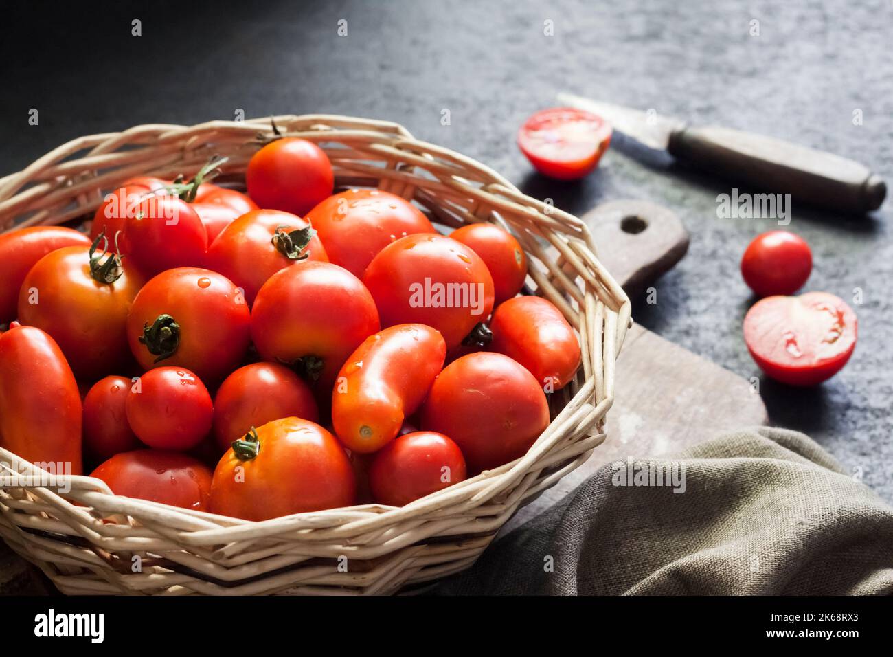 Fresh red tomatoes in whicker basket on black background. Stock Photo