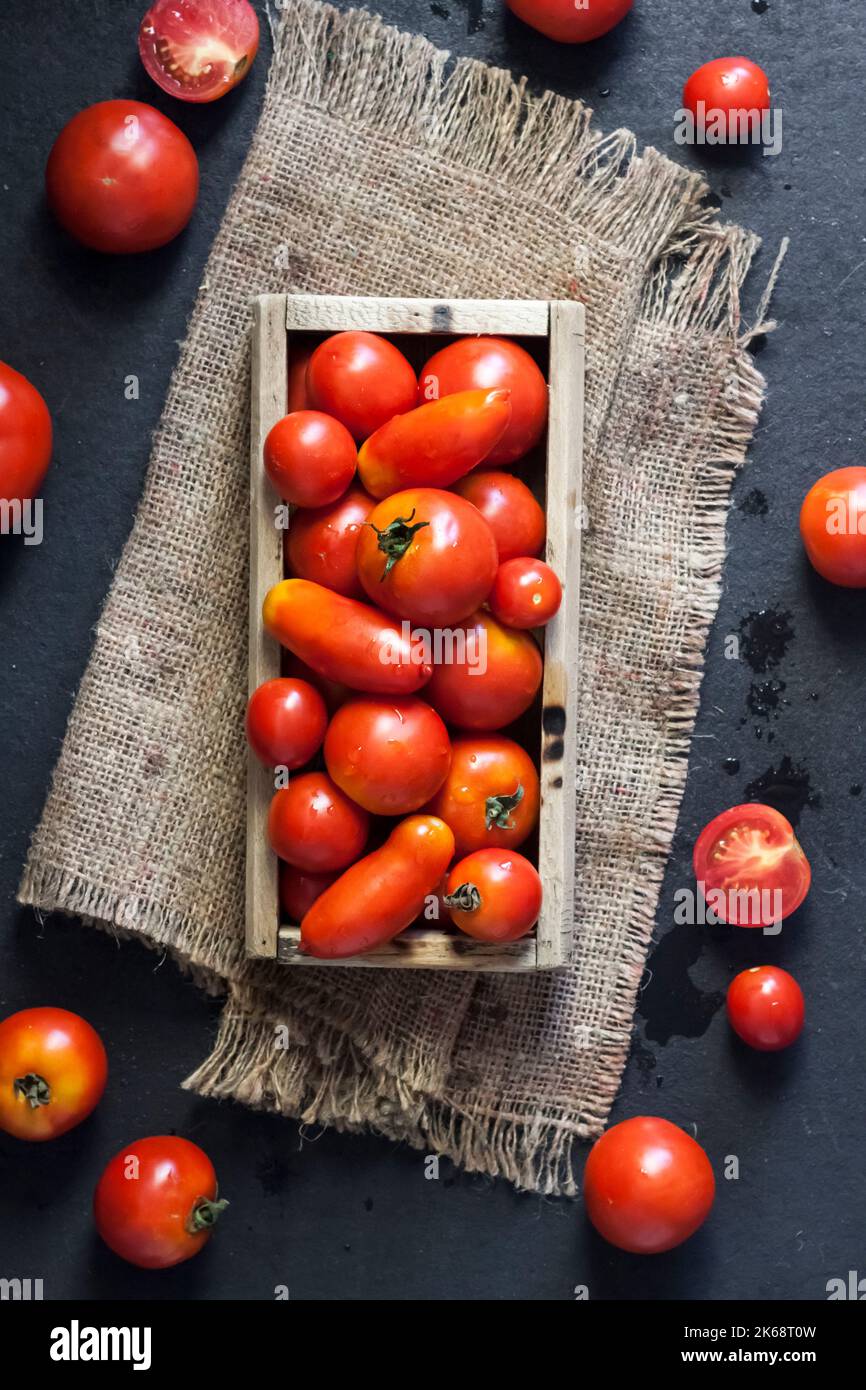 Fresh red tomatoes in wooden box on black background. Flat lay, top view Stock Photo