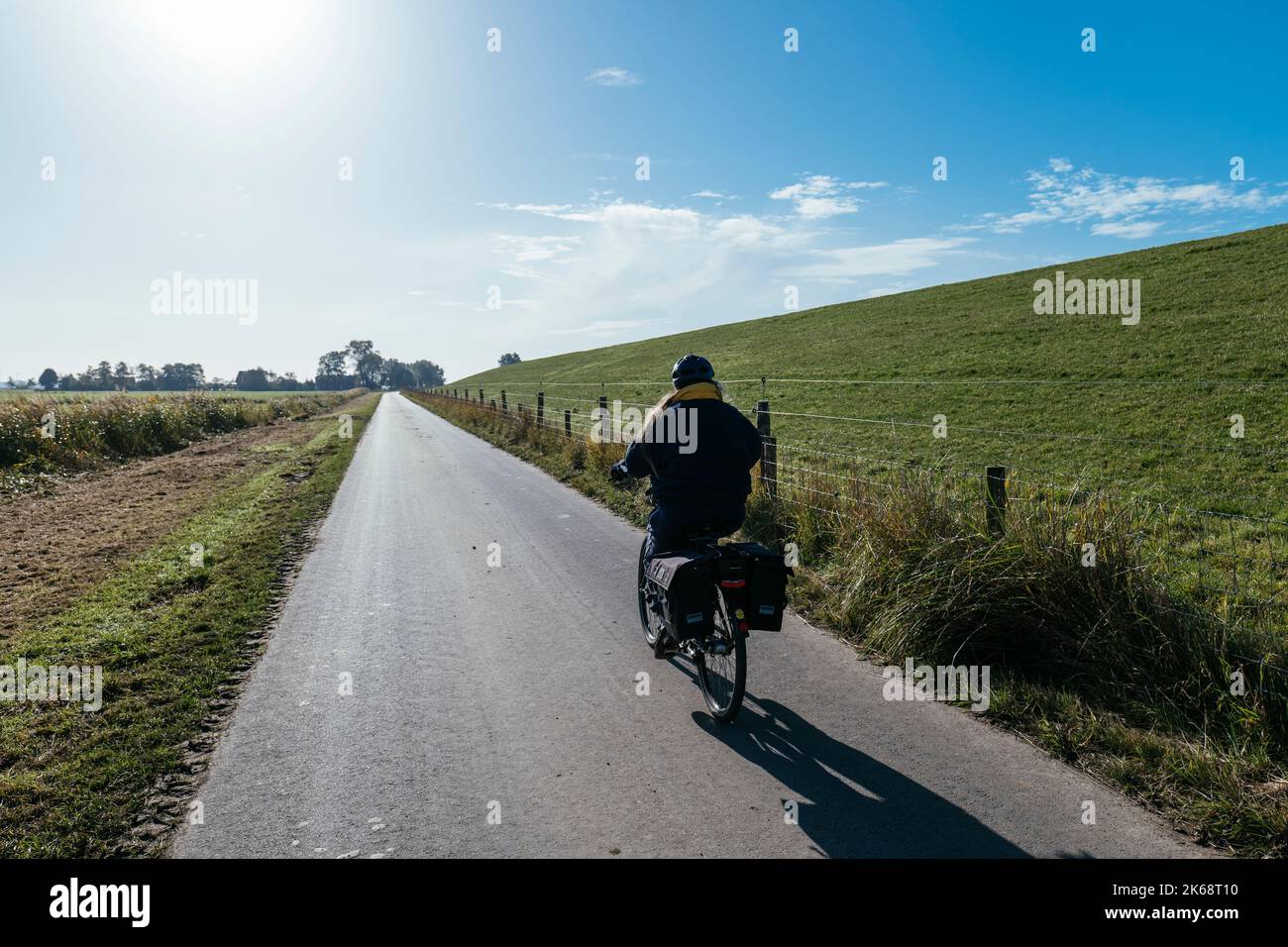 Woman on a bicycle behind the levee on the Weser cycle path south of Bremerhaven. Stock Photo