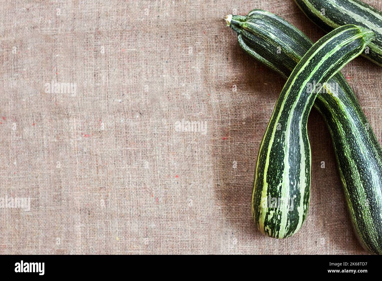Fresh striped zucchini on sackcloth background with copy space. Flat lay, top view. Rustic style Stock Photo