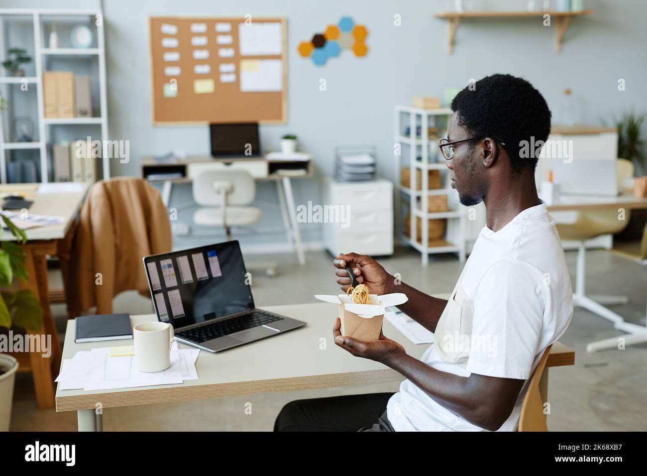 Side View Portrait Of Young Black Man Eating Takeout Noodles At Side View Portrait Of Young Black Man Eating Takeout Noodles At