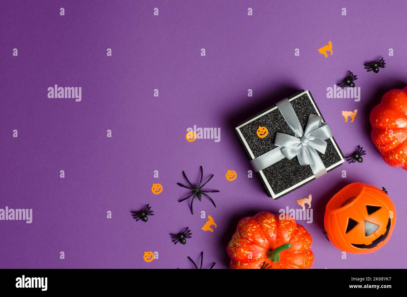 Halloween gifts and sale. Black gift box and traditional halloween decorations on purple background, copy space. Stock Photo