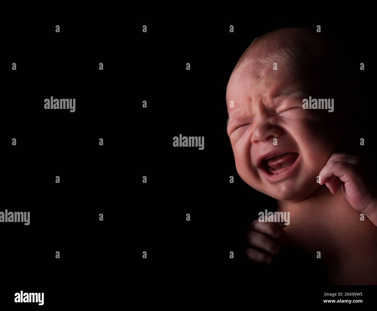 Baby boy with a crying expression in a dark looking environment. Stock Photo