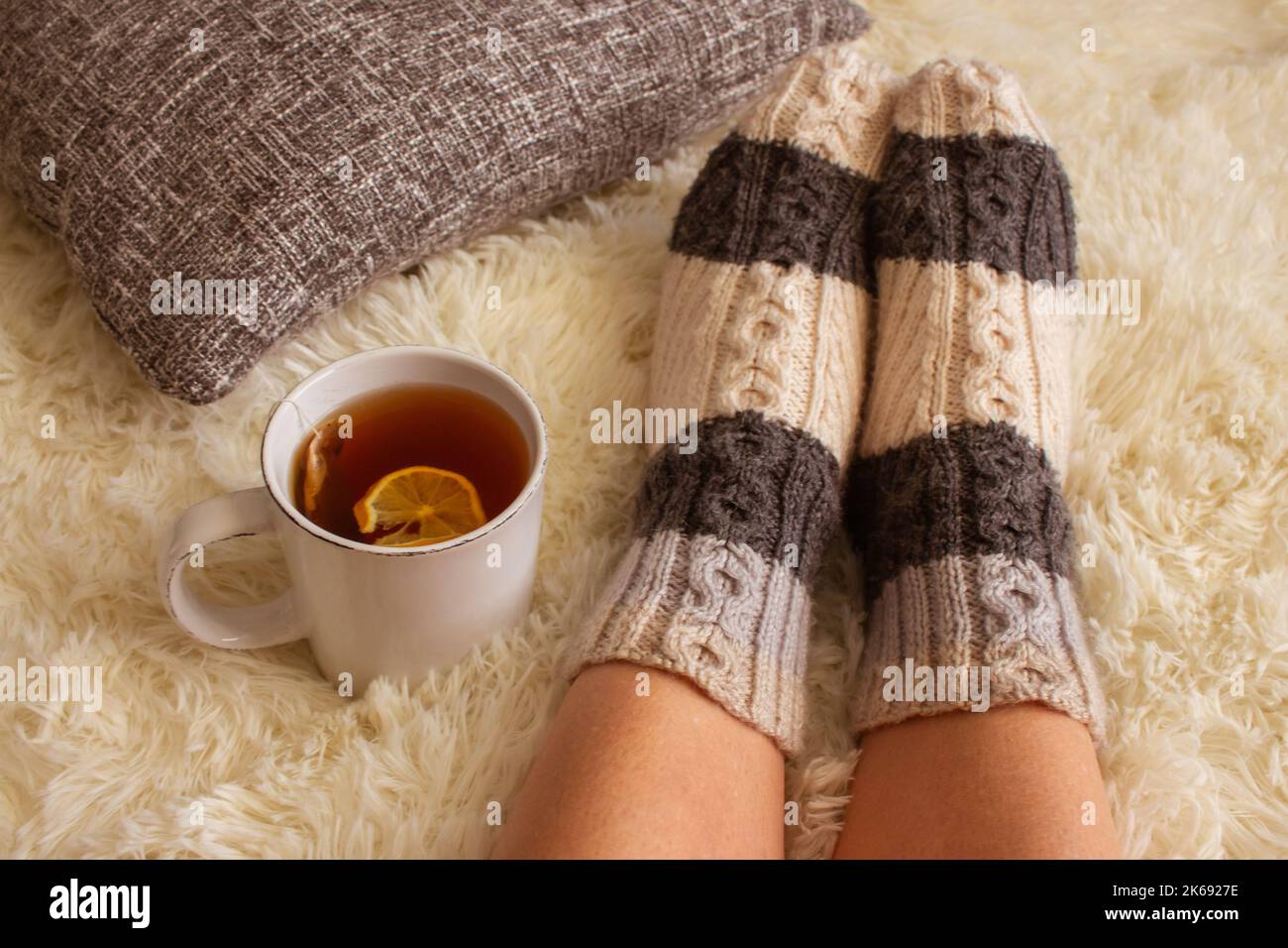 Girl in warm woolen socks with teacup, top view. Woman on white carpet with cup of tea with lemon. Cozy home interior. Winter holidays. Home comfort. Stock Photo