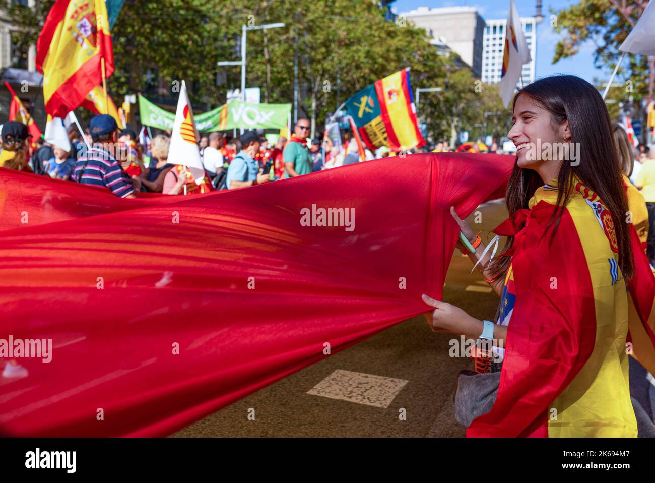 A young woman smiles while holding a big flag of Spain during the Hispanic Day parade. Hispanic