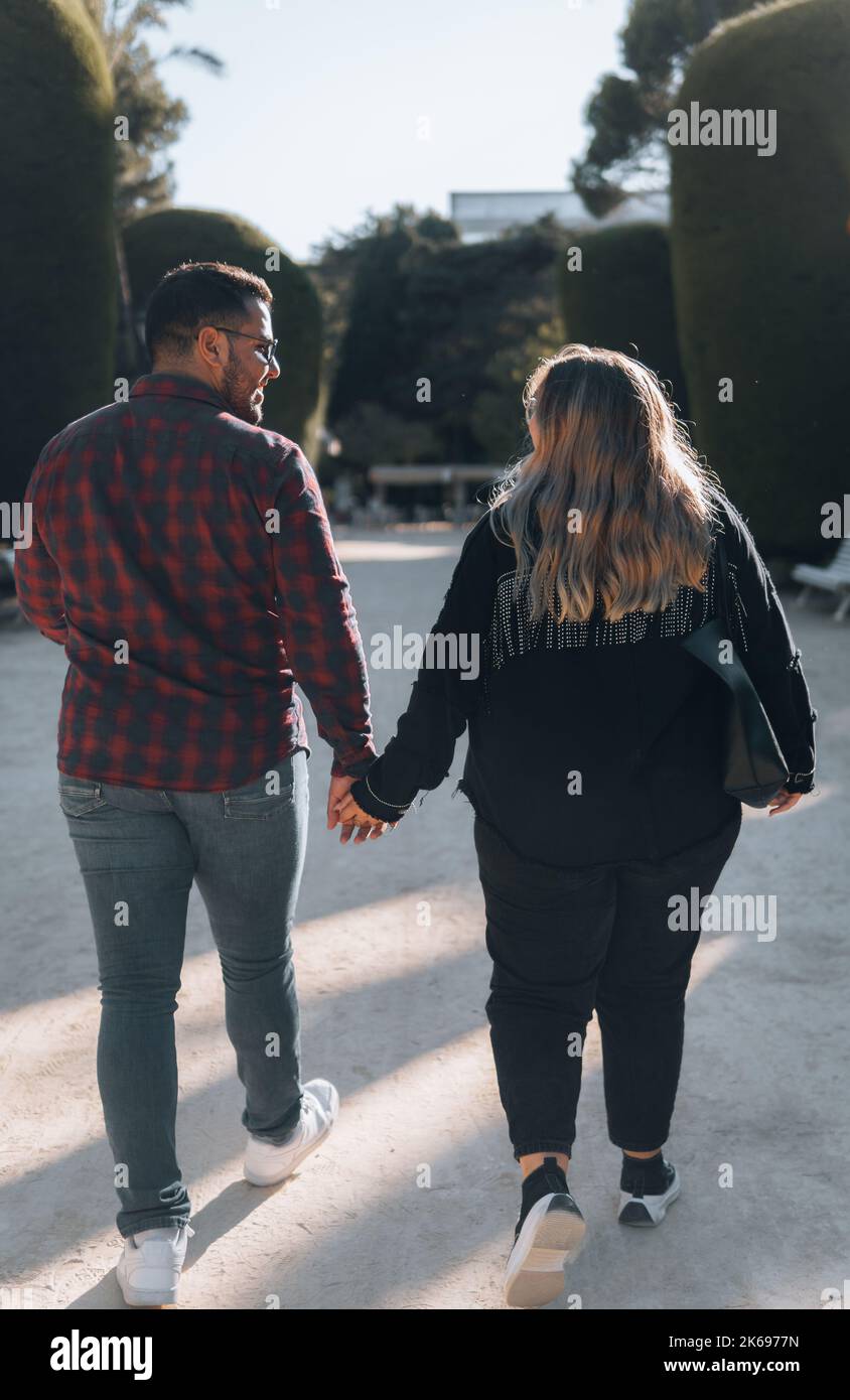 A shallow shot from the back view of a couple walking, holding hands ...