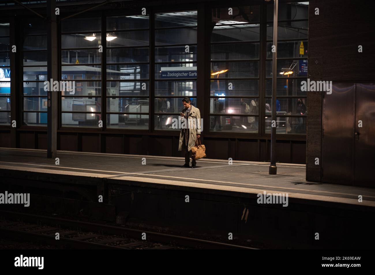 07.10.2022, Berlin, Germany, Europe - A man looks at his mobile phone as he waits for the train on a platform at Bahnhof Zoologischer Garten station. Stock Photo