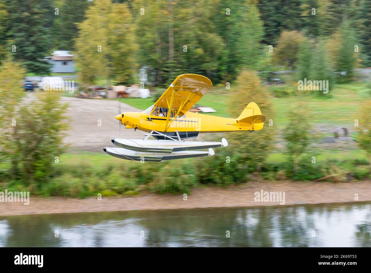 Yellow bush float plane flying over river in Alaska Stock Photo